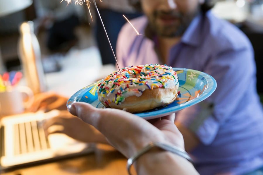 Coworker serving creative businessman birthday donut with sparkler